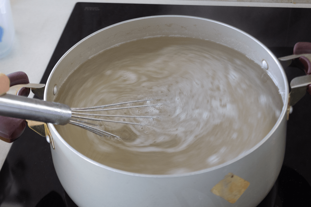 Coconut water in a pot with a whisk in it.