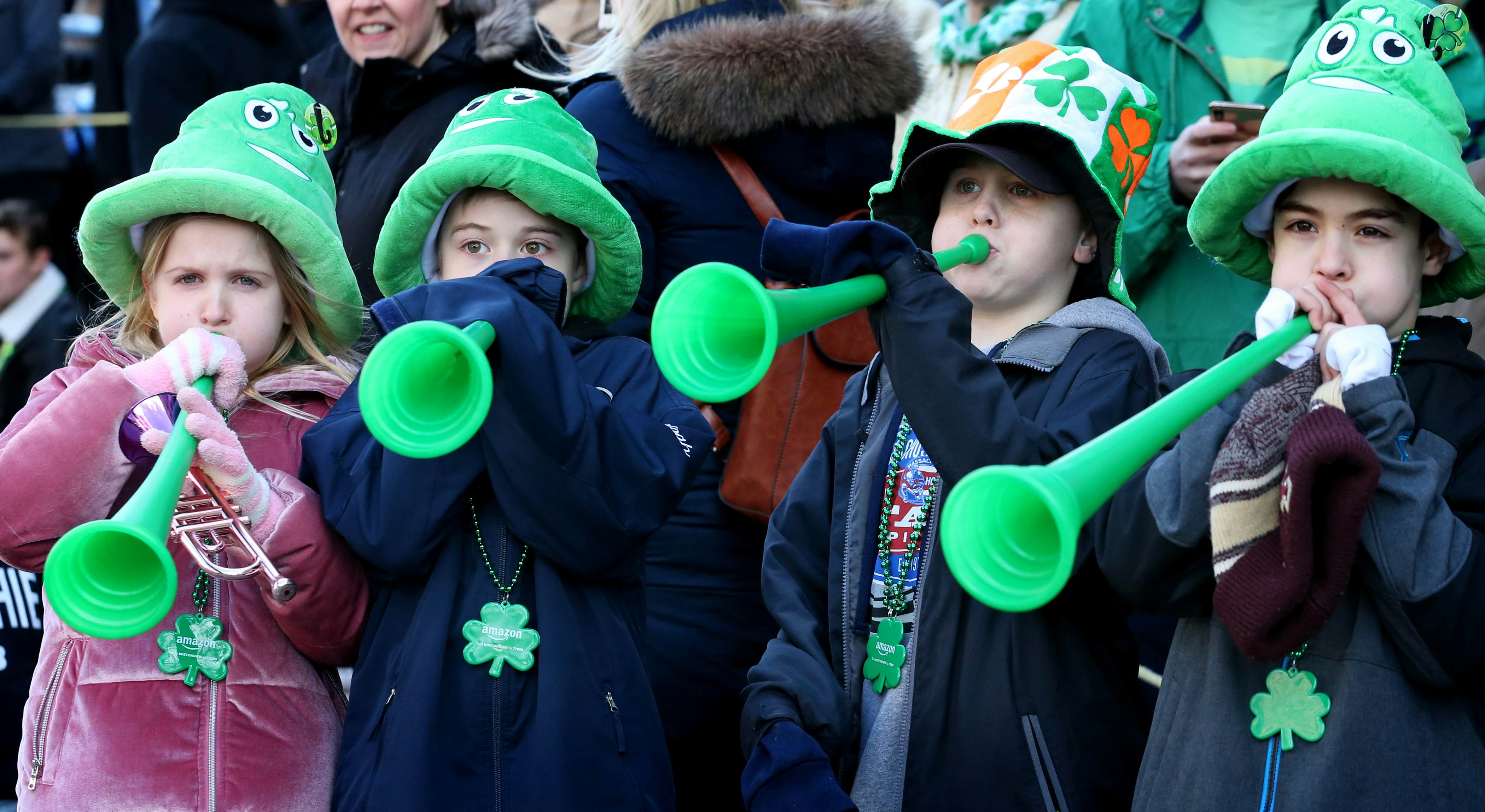 A group of young kids wearing bright green hats blow from green plastic horns during the St. Patrick's Day parade in Boston.