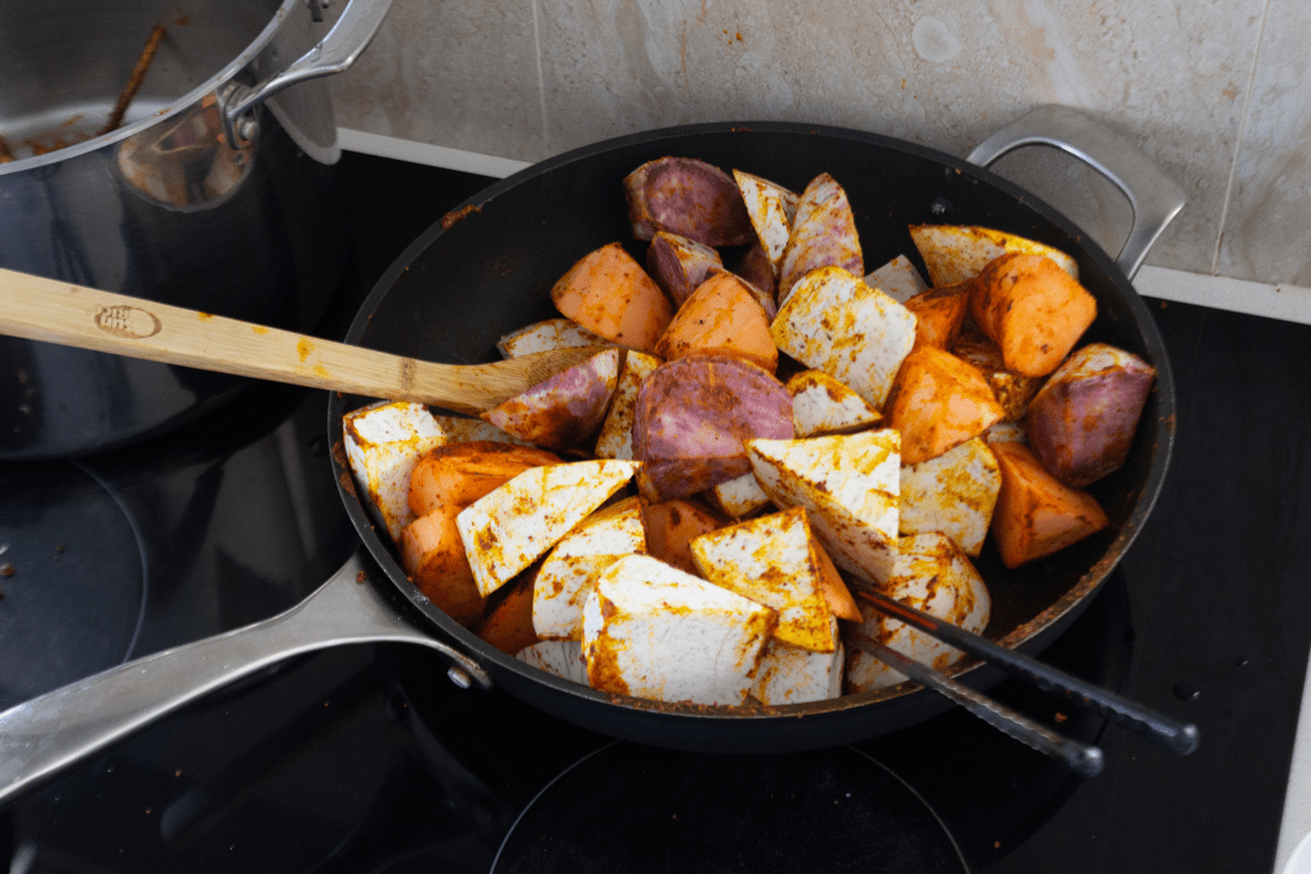 Sweet potato and taro chunks in a pan with chopsticks and a wooden spoon.